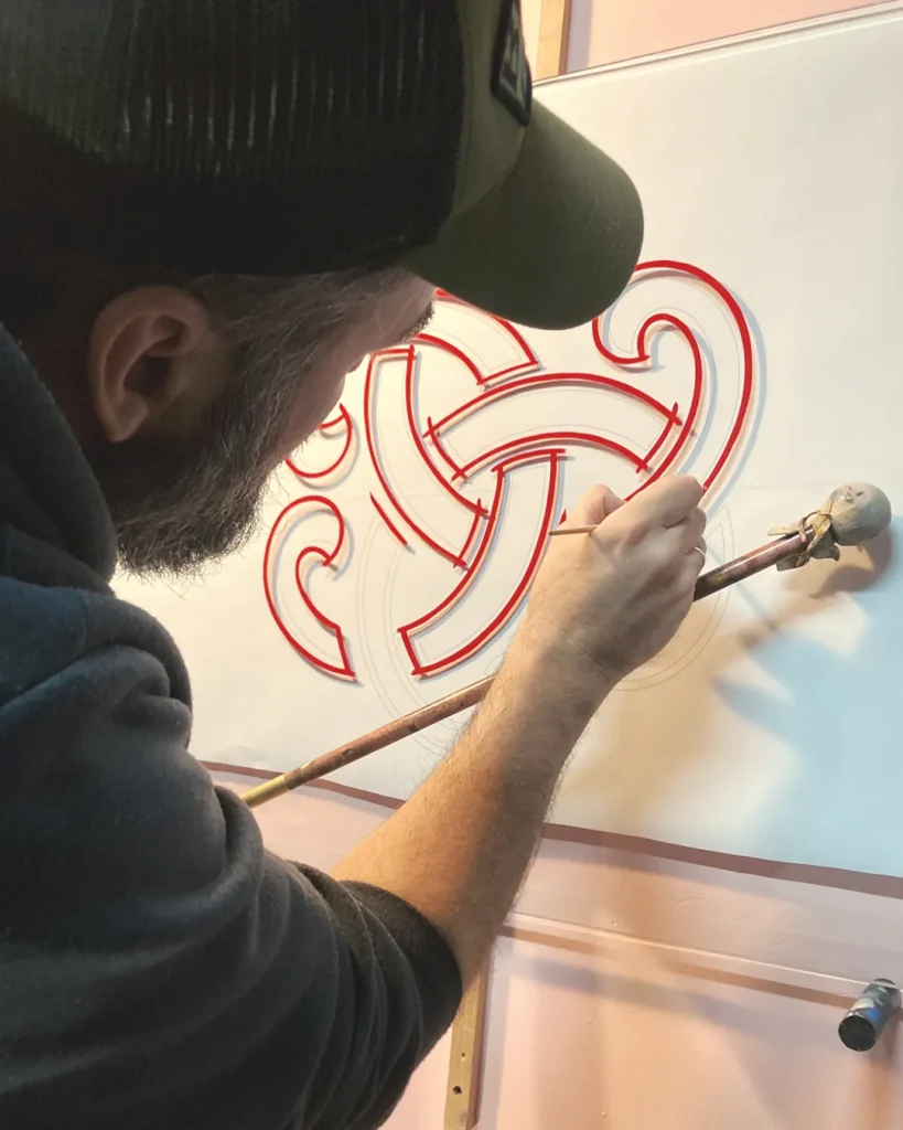 Proceso de rotulación tradicional a mano sobre vidrio realizando el delineado previo para rótulo publicitario con pan de oro