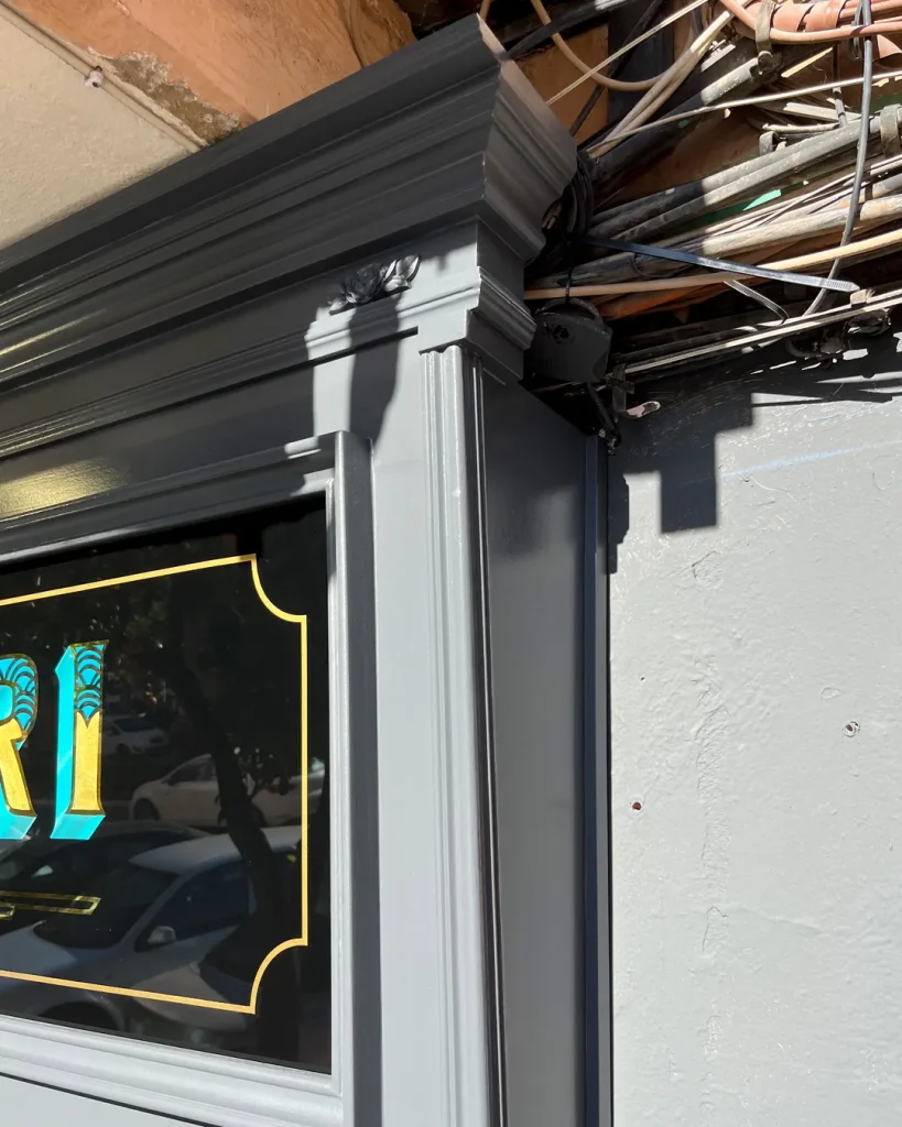 Detalle de moldura decorativa en rótulo tradicional de madera diseñada para ocultar cableado en fachada de estudio de tatuajes en Valencia