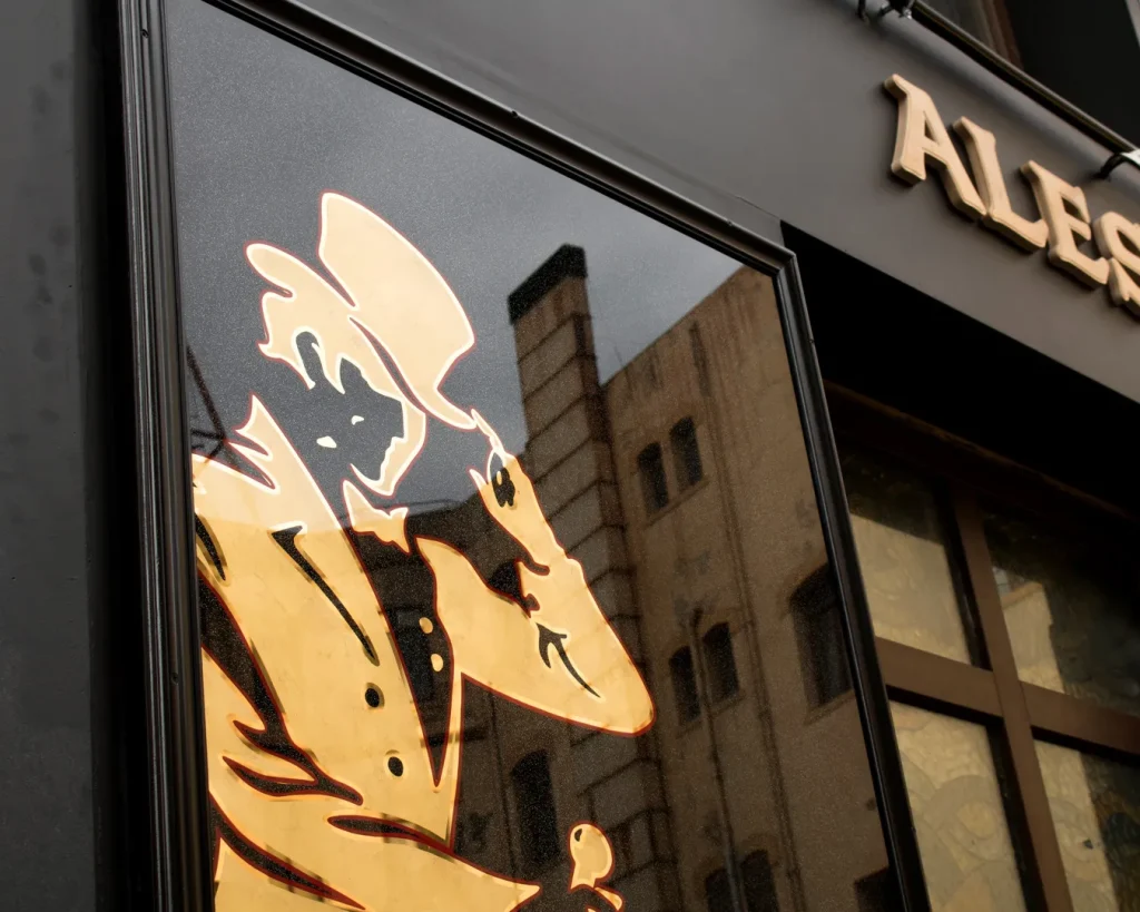 Logotipo de Johnnie Walker rotulado a mano con pan de oro sobre vidrio en rótulo tradicional publicitario