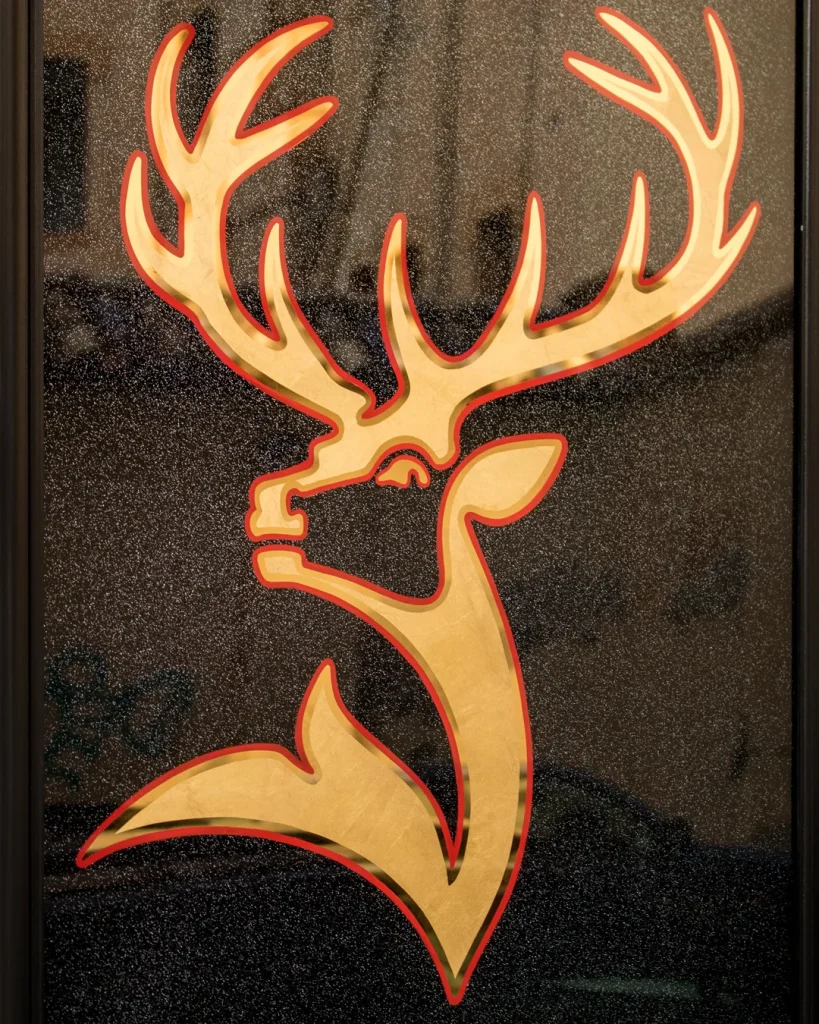 Logotipo de Jägermeister rotulado a mano con pan de oro sobre vidrio en rótulo tradicional publicitario