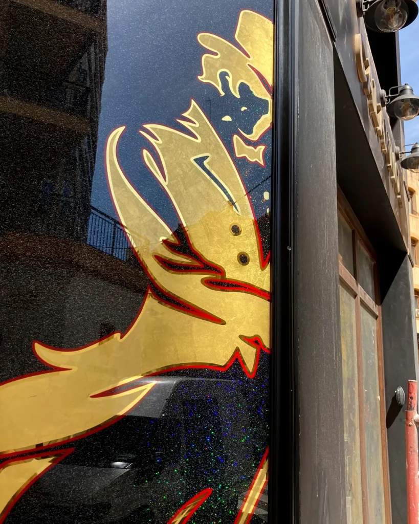 Detalle de rótulo tradicional pintado a mano sobre vidrio con pan de oro y fondo negro con efecto brillante al sol