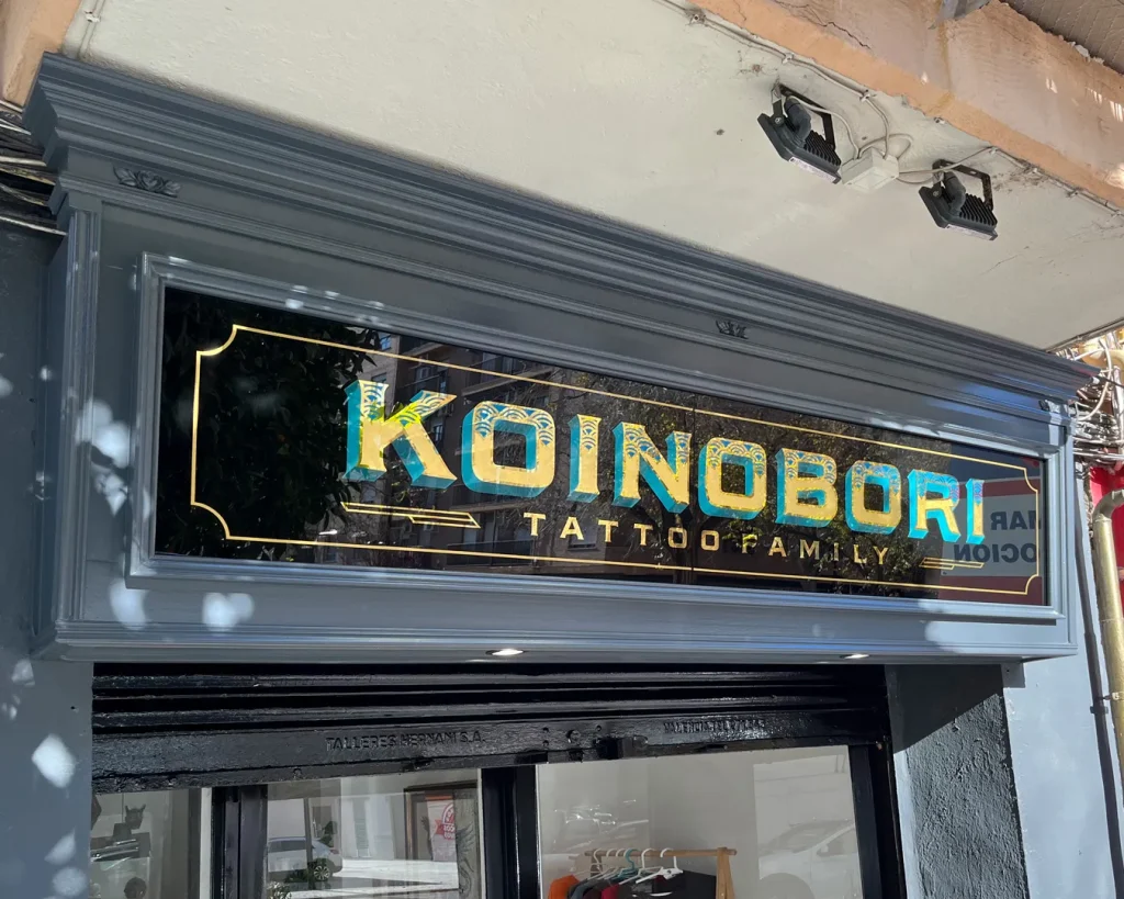 Rótulo tradicional de madera tipo cajón inclinado con vidrio rotulado a mano y pan de oro para estudio de tatuajes en Valencia