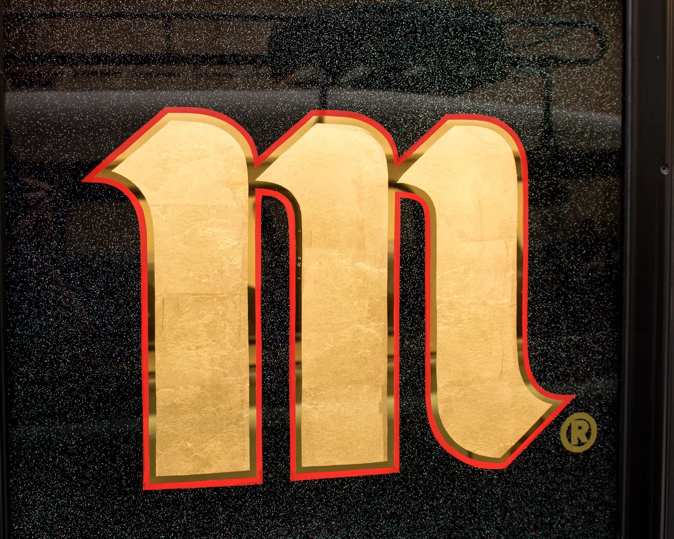 Detalle de la textura del pan de oro mate aplicado a mano sobre vidrio en rótulo tradicional